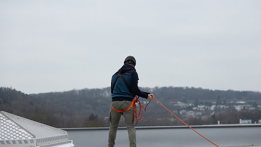 A man wearing anti-fall PPE stands at a fall edge next to a skylight.