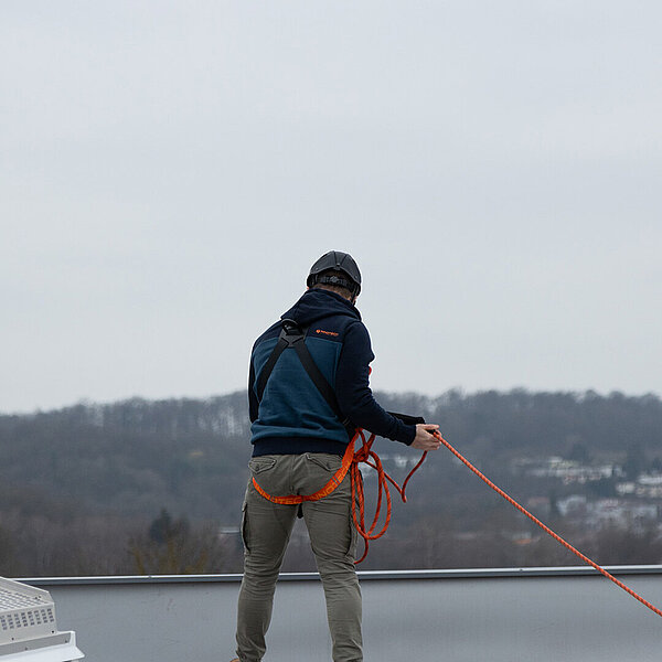 A man wearing anti-fall PPE stands at a fall edge next to a skylight.